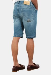 Shorts in denim blu con una finitura sbiadita, design a cinque tasche e una toppa rettangolare in pelle sul retro, abbinati a scarpe da barca marroni.