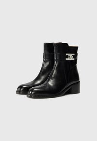 Bottines noires en cuir avec une finition lisse, bouts carrés et un petit talon bloc. Présente un accent de boucle en argent sur la sangle.