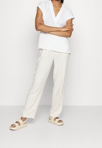 Vit, kortärmad, v-ringad topp kombinerad med ljusbeiga, löst sittande byxor och ljusbruna sandaler med två breda remmar.