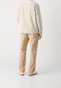 Jasny beżowy żakiet z kołnierzem, zestawiony z khaki spodniami i białymi trampkami z brązowymi podeszwami, widok z tyłu.