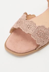 Blush pink sandal med en ruskindsstruktur, der har en scalloped broderet rem og en flad sål. Åben tå-design med minimalistiske detaljer.