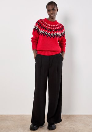 Maglione rosso lavorato a maglia con un giogo decorato in nero, bianco e grigio. Abbinato a pantaloni neri larghi e stivali neri robusti.