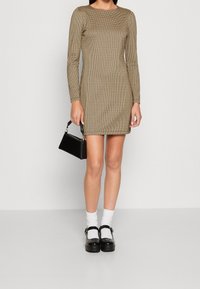 Robe ajustée à manches longues dans un motif à carreaux beige et noir, assortie à un petit sac à main noir et des chaussures à plateforme noires avec des chaussettes blanches.