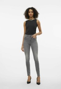 Top negro sin mangas combinado con jeans ajustados gris claro. La tela texturizada, el diseño entallado y los zapatos de tacón altos negros complementan el look.