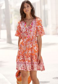 An orange floral dress with short flutter sleeves, a v-neckline, and a tiered skirt, features pink and white patterns and a smocked waist.