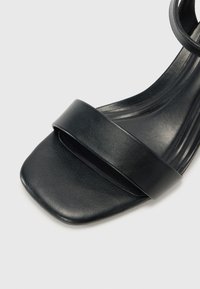 Sandal in pelle nera con punta quadrata, caratterizzato da una larga fascia anteriore e una sottile fascia per la caviglia, dalla texture liscia.