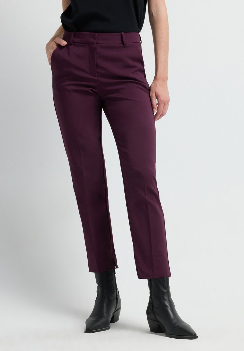 Pantalones de corte entallado burdeos, con una textura suave, bolsillos frontales y una pequeña abertura en el dobladillo, combinados con botines negros.
