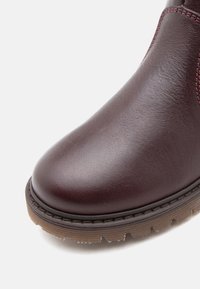 Bottines en cuir bordeaux avec un bout rond, surface texturée, coutures contrastées et semelle en caoutchouc avec bords crantés.