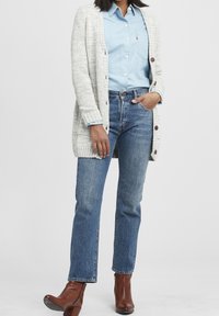 Ljusa grå stickade koftor över en blå denimskjorta, tillsammans med raka blå jeans och bruna klackade ankelskor.