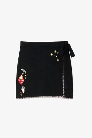 Black wrap skirt with embroidered details including stars, a heart, a hand, and a flower. Finished with contrasting stitched hem and tie.