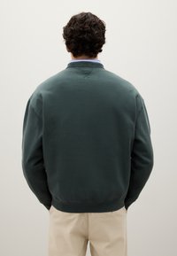 Felpa in cotone verde scuro con colletto rotondo, polsini e orlo a coste. Presenta un taglio classico con una texture liscia e dettagli minimi.
