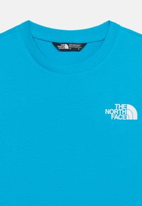 Φωτεινό μπλε t-shirt με στρογγυλή λαιμόκοψη, με λευκό λογότυπο "The North Face" στο αριστερό στήθος και μαύρη ετικέτα μεγέθους μέσα στη γιακά.