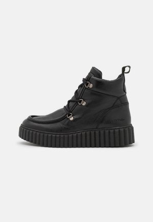 Czarny wysokogatunkowy sneaker z grubą, karbowaną podeszwą, metalowymi oczkami i pętelką na pięcie, pokazany z profilu bocznego.