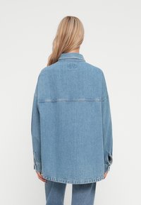 Giacca di jeans blu chiaro con vestibilità ampia, caratterizzata da un colletto a punta, maniche lunghe e orlo dritto. Dettagli di cucitura delicati sulle cuciture.