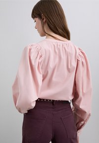 Lichtroze shirt met lange mouwen en opgepofte schouders, met een ronde halslijn. Gecombineerd met donkerpaarse, nauwsluitende broek, met rugontwerp.