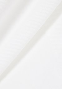 Tissu blanc avec un motif subtil de tissage diagonal, doucement drapé pour créer des ombres légères et des variations de texture.