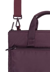 Sac à épaule en nylon violet avec une bandoulière amovible, des poignées supérieures, une poche zippée à l'avant et des coutures contrastées. Texture lisse.