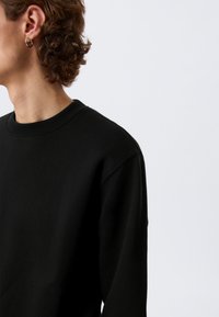 Sweat-shirt noir à col rond, fabriqué en tissu doux, doté d'une coupe décontractée et d'épaules légèrement tombantes pour plus de confort.