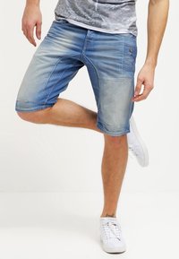 Vaaleansinisiä farkkushortseja, joissa on kulutettuja yksityiskohtia. Niissä on kapeahko malli, polvimittainen leikkaus ja kontrastiväriset ompeleet. Yhdistettynä valkoisiin tennareihin.