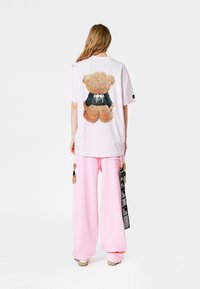 Camiseta rosa de gran tamaño con un gráfico de un oso de peluche en la parte de atrás. Combinada con pantalones rosa holgados que presentan detalles de osos de peluche.