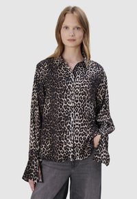 Leopardprint button-up shirt in zwart en beige, met lange mouwen met uitsparingen en een relaxte pasvorm. Draagt het met grijze jeans.