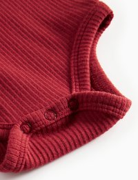 Tessuto bordeaux a costine con una texture morbida; presenta un collo rotondo e tre bottoni a pressione lungo l'orlo inferiore.