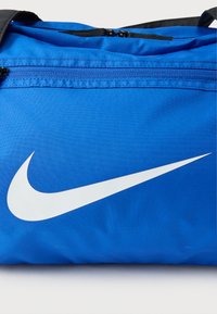 Μπλε νάιλον τσάντα duffle με μαύρες λεπτομέρειες, που διαθέτει μεγάλο λευκό λογότυπο Nike Swoosh και επάνω κλείσιμο με φερμουάρ. Ομαλή υφή.