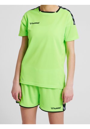 Person iført neongrønt sportstøj med sorte detaljer, inklusive en kortærmet skjorte og shorts, begge med Hummel-logo.