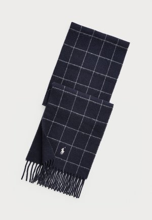 Écharpe en laine bleu marine avec un motif à carreaux blancs, bords frangés et petit logo blanc brodé près du coin.