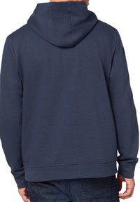 Granatowa bluza z kapturem o gładkiej, teksturowanej tkaninie. Posiada długie rękawy i ściągacz u dołu. Brak widocznych logotypów lub wzorów. Widok z tyłu.