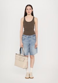 Top con spalline marrone, pantaloni denim, borsa tote beige con accenti neri, sneakers, calze bianche e capelli lisci su uno sfondo neutro.