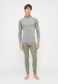 Haut à manches longues gris à côtes avec un col montant, assorti à des leggings olive ajustés. Texture lisse, design minimal, sans motifs visibles.