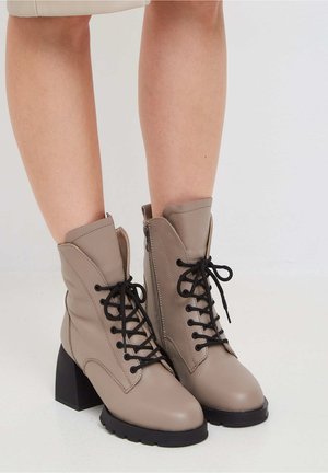 Beige veterlaarzen tot de enkels met een chunky zwarte hak en een gestructureerde zool. Voorzien van een ritssluiting en een gladleren bovenkant.