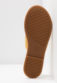 Chaussure jaune avec une semelle en caoutchouc texturée, dotée d'une surface adhérente à motifs et d'un bout arrondi. Taille indiquée comme 37 sur la semelle.