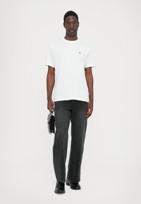 Hvit T-skjorte med korte ermer og rund hals samt liten logo. Mørkegrå, rette jeans med sidestriper. Svarte sko og liten veske.