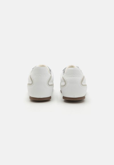 Zapatillas de cuero blancas con una suela de goma marrón, que presentan detalles del logo en el talón y costuras en contraste a lo largo de los lados.