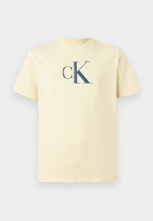 T-shirt en coton jaune clair avec un logo "ck" bleu marine centré sur la poitrine, col rond et manches courtes.