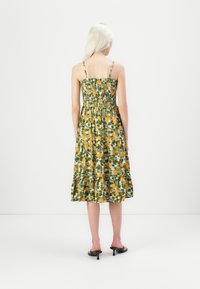 Robe florale verte avec des accents jaunes, corsage smocké et jupe à volants. Fines bretelles et design mi-long, faite en tissu léger.