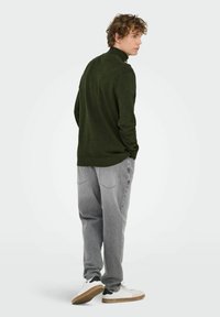 Dunkelgrüner strukturierten Rollkragenpullover, kombiniert mit hellgrauen locker sitzenden Jeans und weißen Sneakers mit schwarzen Akzenten. Schlichtes Design, lässiger Stil.