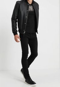 Zwarte leren bomberjack, zwart t-shirt met graphic, zwarte slim-fit jeans en zwarte sneakers met witte zolen. Eenvoudig, casual ontwerp.