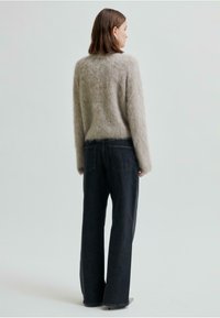 Grå mohairtröja med en mjuk, fluffig textur som passar med högmidjade mörka denimjeans. Outfiten har vida ben och subtila fickdetaljer.