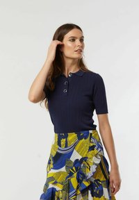 Marineblauwe geribbelde polo met korte mouwen en een drieknoopssluiting, gecombineerd met een meerkleurige, gestreepte rok met bloem- en loofontwerpen.