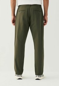 Olive green trousers with a straight fit, made of soft fabric, featuring double back pockets with button closures, paired with grey sneakers.