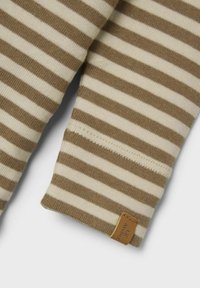 Camicia a maniche lunghe a righe marroni e crema, realizzata in un tessuto texture e con un piccolo etichetta in pelle sul polsino. I polsini presentano dettagli di cucitura visibili.