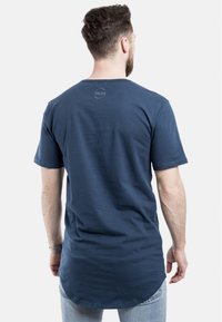 Tamsiai mėlyna trumpa rankovė T-shirt, pagaminta iš medvilnės, su apvalia apačia ir maža logotipo siuvinėjimu nugaros iškirpėje.