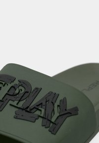 Πράσινο σανδάλι με λουράκι από υφή ελαστικού που φέρει ανάγλυφα μαύρα γράμματα «PLAY». Λείος πάτος με μινιμαλιστικό σχέδιο.