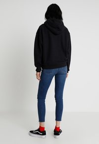 Sweat à capuche noir avec cordon de serrage et poche kangourou, associé à un jean skinny bleu et à des baskets noires avec semelles blanches et chaussettes rouges.