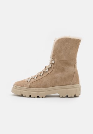 Botte d'hiver en daim brun clair à lacets avec semelle épaisse en caoutchouc beige et doublure en fourrure douce autour de la cheville.