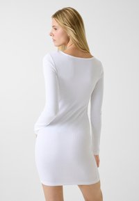Biała sukienka z długim rękawem, wykonana z prążkowanej tkaniny, z okrągłym dekoltem i dopasowanym krojem, sięgająca do połowy uda.