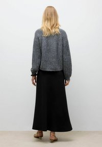 Svetlo sivi pleteni pulover z rebrasto teksturo, skrajšana silhueta, v kombinaciji z črno maksi krilo in bež petkami.
